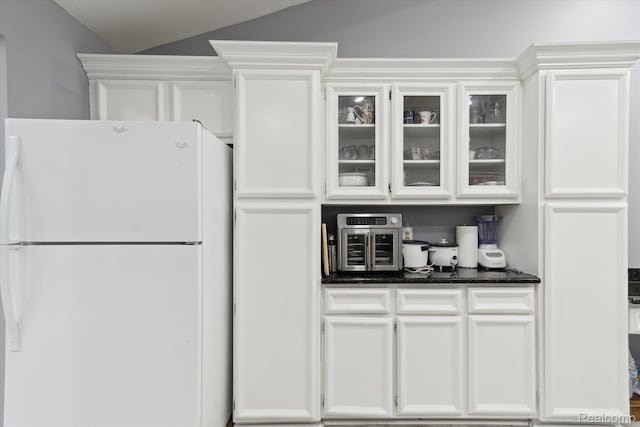 13439 Brougham Dr, Warren, MI 48312 - kitchen featuring freestanding refrigerator, white cabinets, glass insert cabinets, lofted ceiling, and dark stone countertops