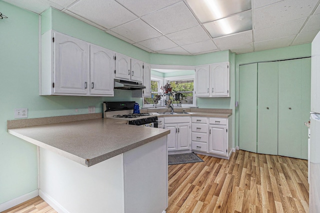 299 5th Ave, Manistee, MI 49660 - kitchen featuring white range oven, white cabinets, a peninsula, light wood finished floors, and a paneled ceiling