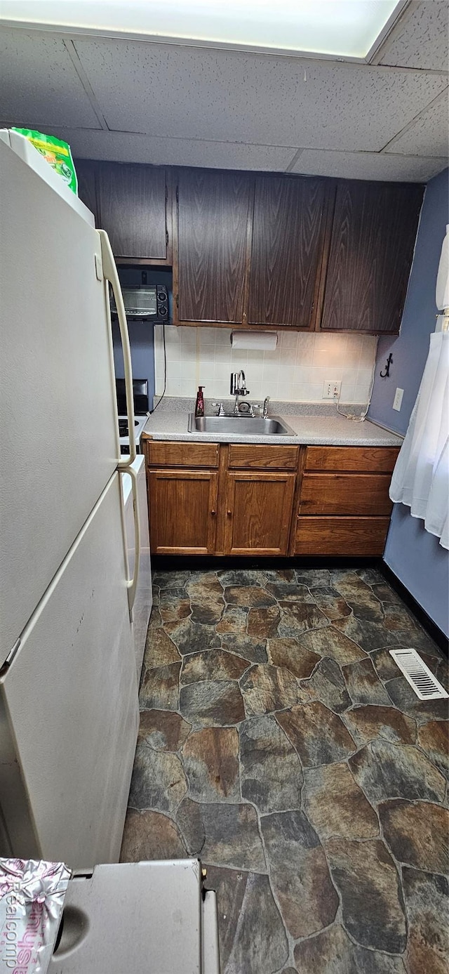 21117 Woodward St, Utica, MI 48035 - kitchen featuring freestanding refrigerator, dark stone finish floors, a drop ceiling, light countertops, and a sink
