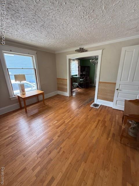 619 W Barnes Ave, Lansing, MI 48910 - empty room featuring wood finished floors, ornamental molding, a textured ceiling, a wainscoted wall, and baseboards