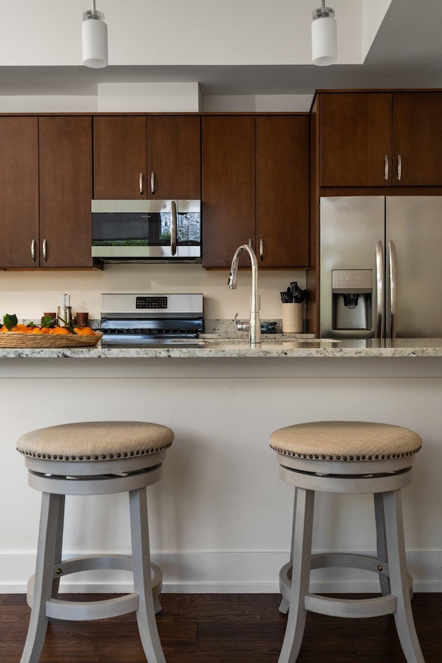 410 N First St Unit 207, Ann Arbor, MI 48103 - kitchen featuring appliances with stainless steel finishes, a breakfast bar area, dark brown cabinets, and light stone countertops