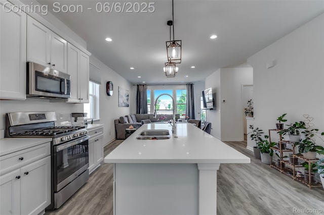 137 Monument Ln, Wixom, MI 48393 - kitchen featuring appliances with stainless steel finishes, open floor plan, light wood finished floors, a kitchen island with sink, and light countertops
