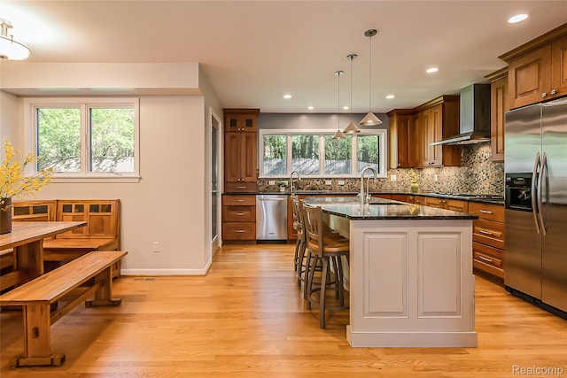 2694 Wayside Dr, Ann Arbor, MI 48103 - kitchen with stainless steel appliances, wall chimney range hood, a kitchen breakfast bar, light wood-style floors, and tasteful backsplash