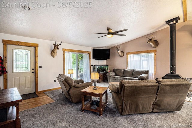 3275 Levalley Rd, Columbiaville, MI 48421 - carpeted living room featuring a wood stove, a textured ceiling, a ceiling fan, lofted ceiling, and baseboards
