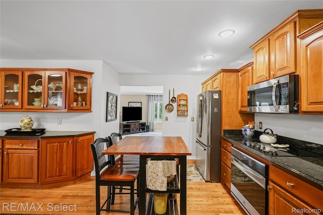 2391 Atwell Rd, Attica, MI 48412 - kitchen featuring appliances with stainless steel finishes, light wood-style flooring, glass insert cabinets, dark stone countertops, and brown cabinets