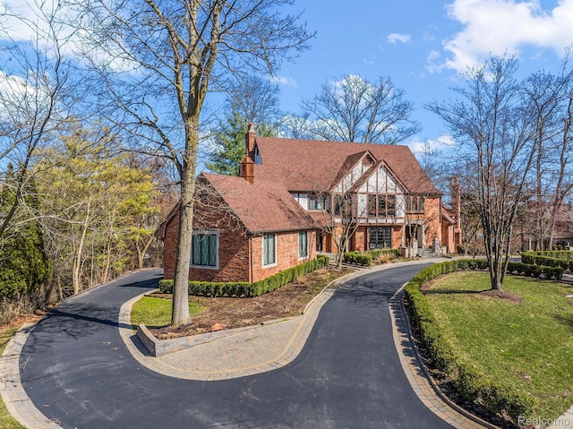 3013 Heron Pl, Bloomfield Hills, MI 48302 - tudor-style house featuring a chimney, driveway, a front lawn, brick siding, and roof with shingles