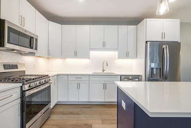 603 Woodland, Dexter, MI 48130 - kitchen featuring appliances with stainless steel finishes, a sink, light wood-type flooring, decorative backsplash, and white cabinetry