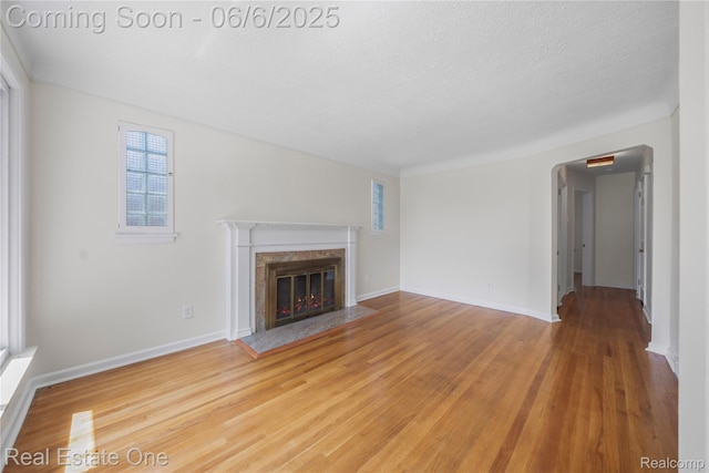 21167 Lancaster St, Grosse Pointe Woods, MI 48225 - unfurnished living room with a high end fireplace, light wood-style flooring, a textured ceiling, baseboards, and arched walkways