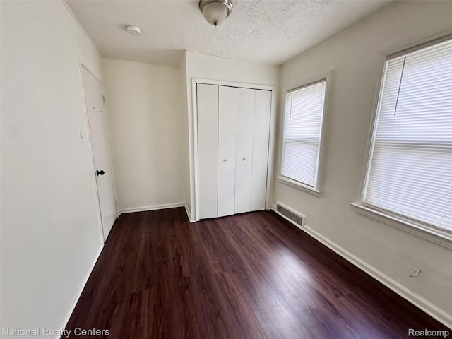 5689 Cornell St, Dearborn Heights, MI 48125 - unfurnished bedroom with dark wood-style flooring, a closet, multiple windows, baseboards, and a textured ceiling
