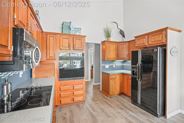 7457 Haviland Beach Dr, Argentine, MI 48451 - kitchen with black appliances, decorative backsplash, brown cabinetry, a high ceiling, and light wood-style floors