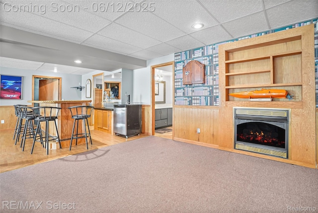 7457 Haviland Beach Dr, Argentine, MI 48451 - kitchen featuring a paneled ceiling, a kitchen bar, light carpet, a fireplace, and wooden walls