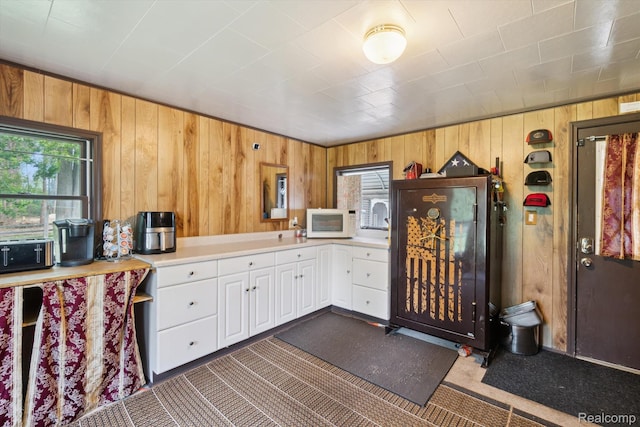 1250 W Thompson Rd, Fenton, MI 48430 - kitchen with white microwave, wooden walls, light countertops, dark carpet, and white cabinets