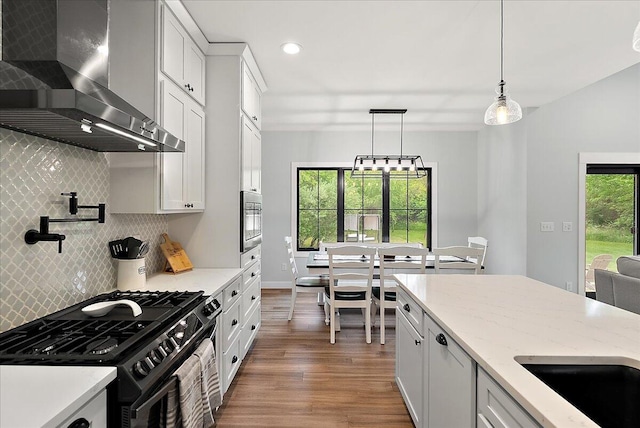 8011 Date Rd, Stevensville, MI 49127 - kitchen with wall chimney exhaust hood, black range with gas stovetop, wood finished floors, tasteful backsplash, and pendant lighting