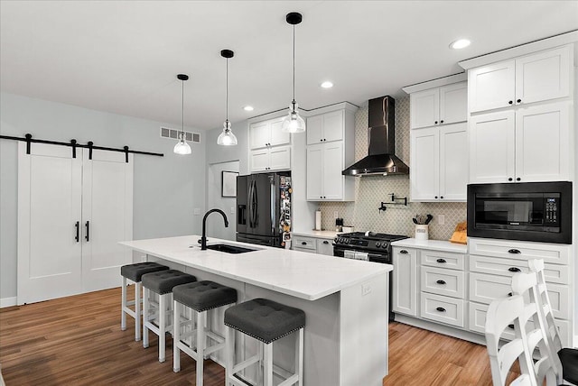 8011 Date Rd, Stevensville, MI 49127 - kitchen featuring black appliances, wall chimney exhaust hood, a sink, a center island with sink, and light wood-style flooring