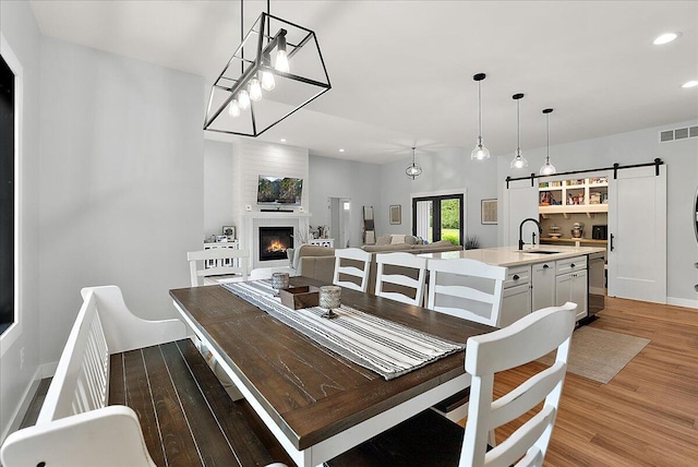 8011 Date Rd, Stevensville, MI 49127 - dining area with a barn door, light wood-type flooring, a lit fireplace, recessed lighting, and baseboards