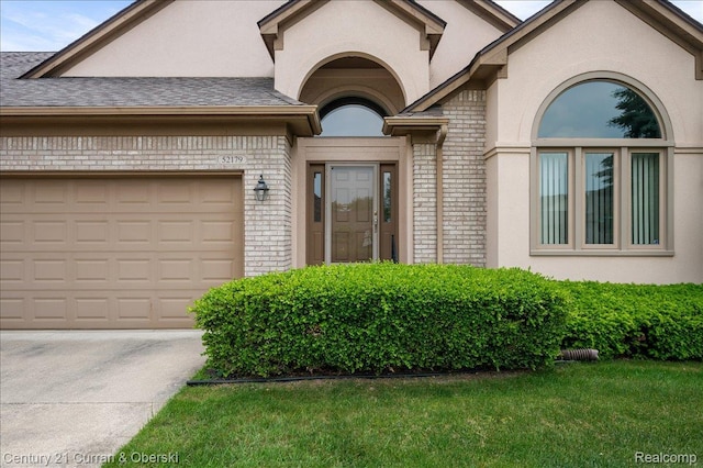 52179 Sawmill Creek Dr, Macomb, MI 48042 - view of exterior entry featuring brick siding, driveway, an attached garage, a yard, and a shingled roof