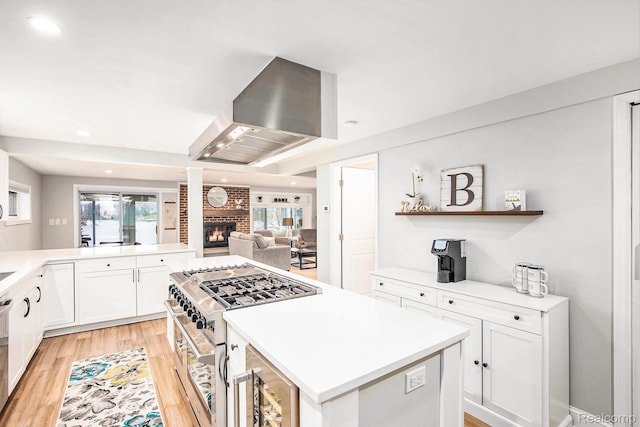 10048 King Rd, Davisburg, MI 48350 - kitchen with wall chimney exhaust hood, a brick fireplace, a kitchen island, white cabinets, and light wood-style flooring