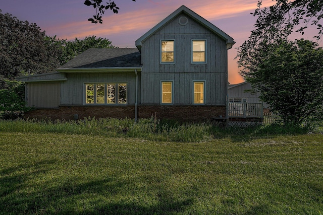 19146 Fairchild Rd, Constantine, MI 49042 - back of house at dusk featuring a lawn, a wooden deck, roof with shingles, and brick siding