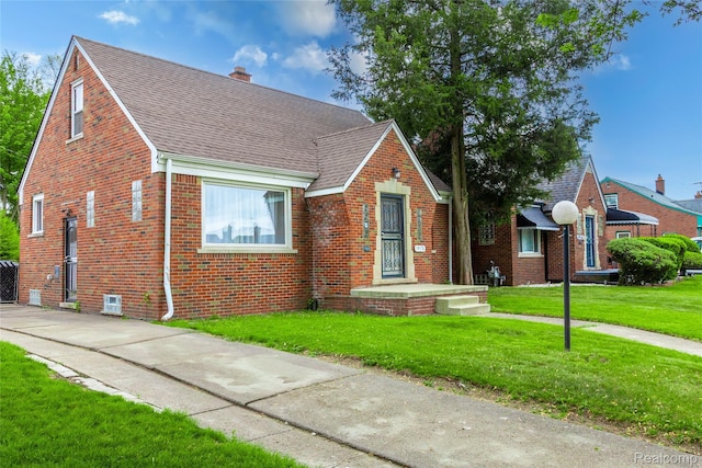 19176 Barlow St, Detroit, MI 48205 - tudor house with brick siding, roof with shingles, a front yard, and a chimney