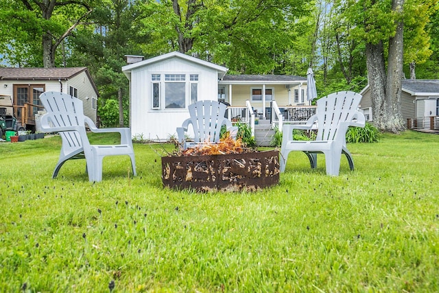 6026 Keeney Rd, Six Lakes, MI 48886 - back of property featuring an outdoor fire pit, a yard, a deck, and view of wooded area