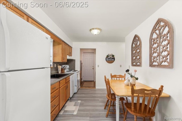 501 Front St, Holly, MI 48442 - kitchen featuring white appliances, light wood finished floors, a sink, dark countertops, and tasteful backsplash