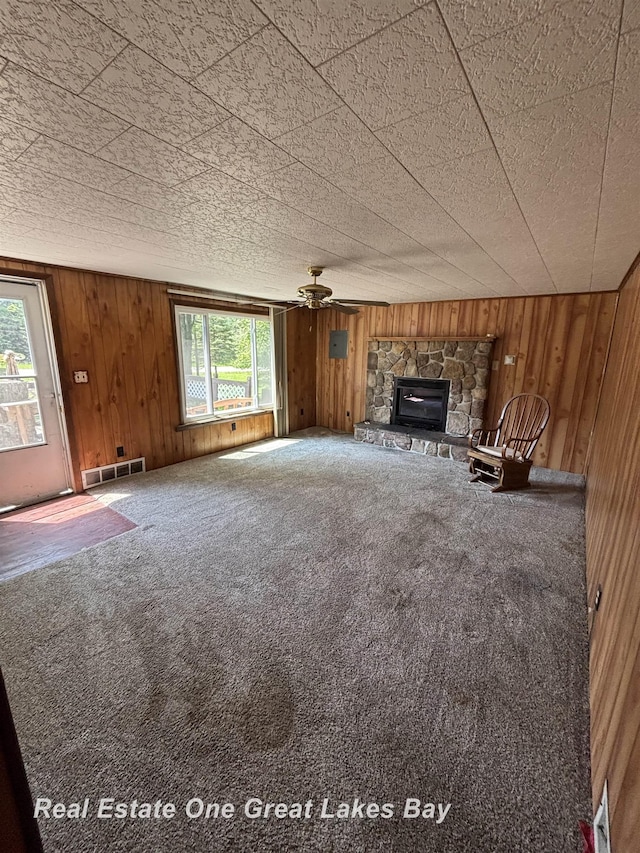 8446 Bamfield Rd, South Branch, MI 48761 - unfurnished living room featuring wooden walls, a ceiling fan, carpet floors, and a fireplace