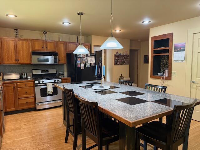 285 Scott St, Newaygo, MI 49337 - kitchen with stainless steel appliances, brown cabinets, a breakfast bar area, decorative light fixtures, and light wood-style flooring