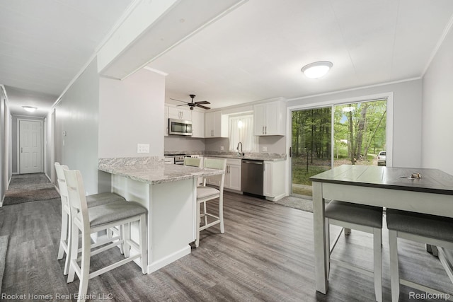 9689 Pine Ln, Evart, MI 49631 - kitchen featuring stainless steel appliances, wood finished floors, a kitchen bar, white cabinetry, and ornamental molding