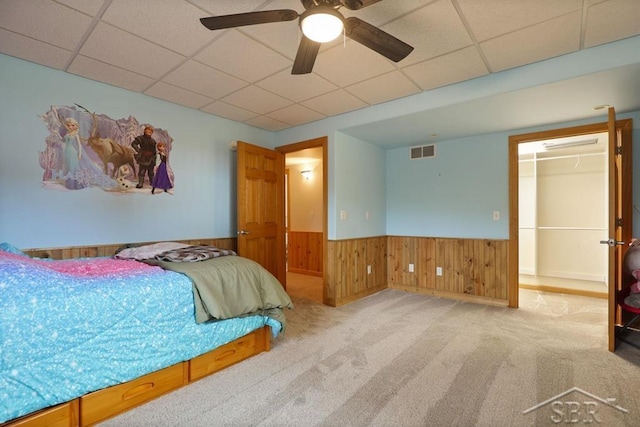 681 Quillett Dr, Beaverton, MI 48612 - carpeted bedroom with a drop ceiling, a wainscoted wall, wooden walls, a walk in closet, and ceiling fan