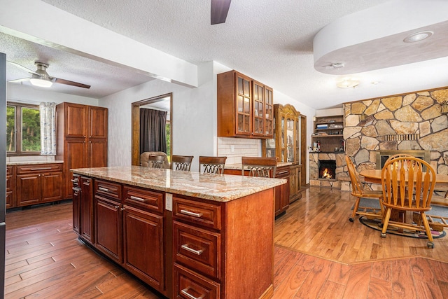 3765 Ryerson Rd, Twin Lake, MI 49457 - kitchen with ceiling fan, a textured ceiling, wood-type flooring, a fireplace, and glass insert cabinets