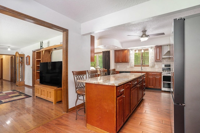 3765 Ryerson Rd, Twin Lake, MI 49457 - kitchen with appliances with stainless steel finishes, a textured ceiling, wall chimney range hood, light wood-style flooring, and a kitchen breakfast bar