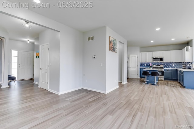 59625 Twin Pines Dr, New Hudson, MI 48165 - kitchen featuring appliances with stainless steel finishes, blue cabinetry, decorative backsplash, light wood-type flooring, and recessed lighting