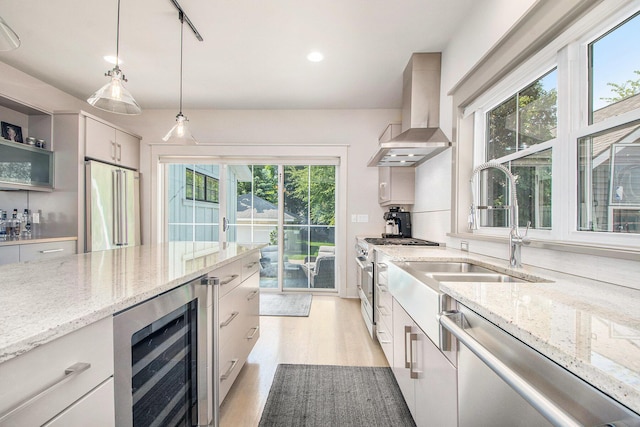 2234 Lake Dr SE, East Grand Rapids, MI 49506 - kitchen with beverage cooler, wall chimney exhaust hood, stainless steel appliances, light wood-type flooring, and pendant lighting