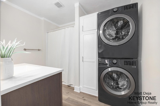 109 Leonard St NE, Grand Rapids, MI 49503 - laundry area featuring stacked washer and clothes dryer, cabinet space, light wood finished floors, and crown molding