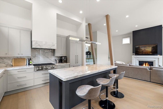 647 Ann St, Birmingham, MI 48009 - kitchen with stainless steel gas stovetop, a breakfast bar, a kitchen island, light stone countertops, and backsplash