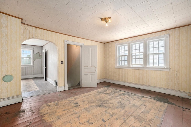 828 Nagold St NW, Grand Rapids, MI 49504 - empty room featuring crown molding, wood-type flooring, arched walkways, wallpapered walls, and baseboards