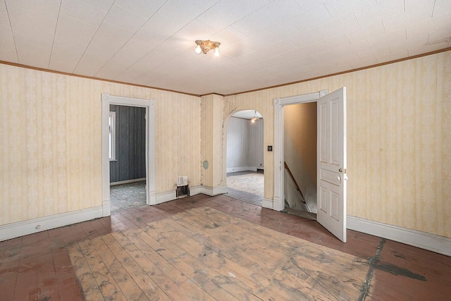 828 Nagold St NW, Grand Rapids, MI 49504 - empty room featuring arched walkways, ornamental molding, dark wood finished floors, wallpapered walls, and baseboards