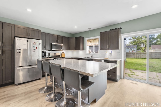 138 E Lake St, Sand Lake, MI 49343 - kitchen with appliances with stainless steel finishes, a kitchen breakfast bar, decorative backsplash, a kitchen island, and dark brown cabinetry