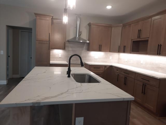 16445 Sleepy Hollow Dr, Fenton, MI 48430 - kitchen featuring wall chimney exhaust hood, decorative backsplash, a kitchen island with sink, light stone counters, and recessed lighting