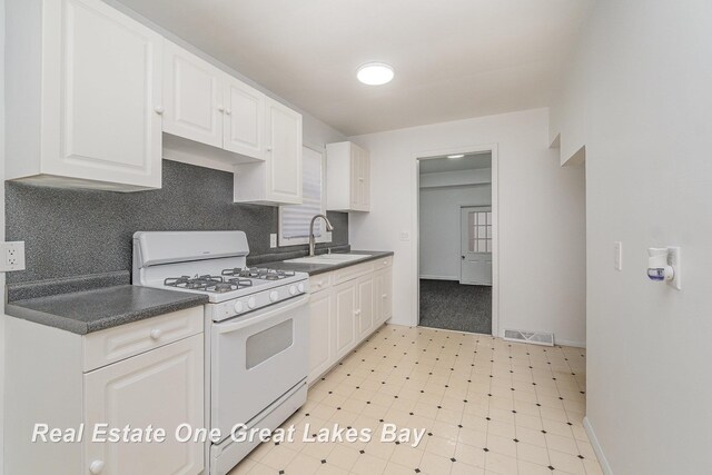 4675 E Parish Rd, Midland, MI 48642 - kitchen with white gas range oven, a sink, decorative backsplash, white cabinetry, and dark countertops