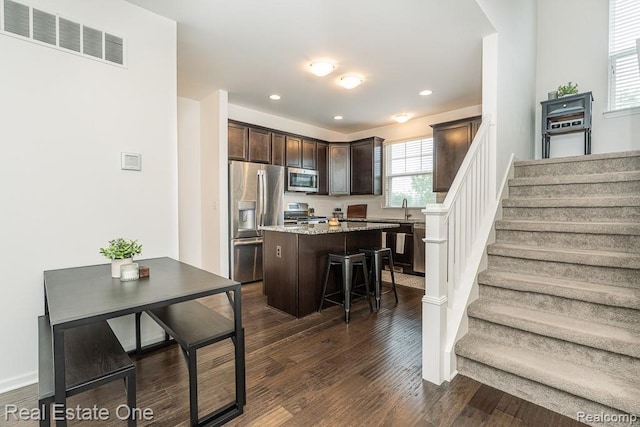 4661 Bradley Cir, Troy, MI 48085 - kitchen featuring stainless steel appliances, dark brown cabinets, a center island, dark wood finished floors, and a breakfast bar