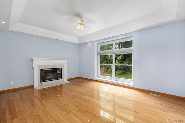 2479 Waterfront Dr, Brighton, MI 48114 - unfurnished living room featuring a raised ceiling, a ceiling fan, wood finished floors, a high end fireplace, and baseboards