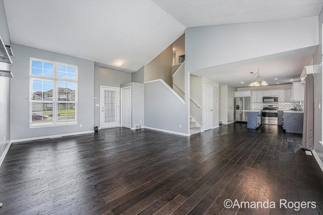 648 Firestone Dr SE, Byron Center, MI 49315 - unfurnished living room featuring dark wood finished floors, stairway, high vaulted ceiling, a chandelier, and baseboards