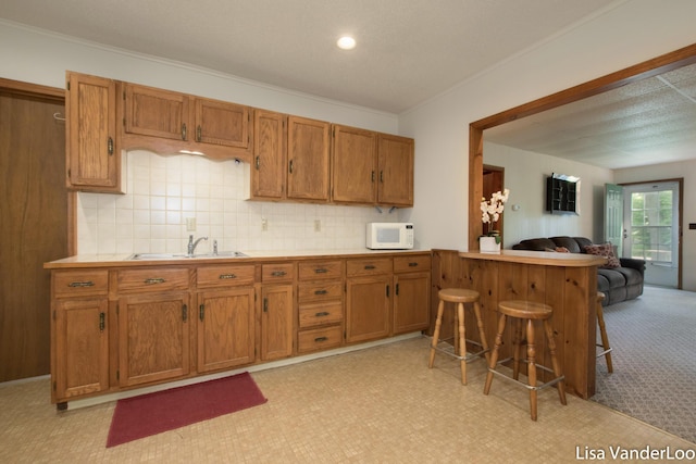 1819 Willis Ave NW, Grand Rapids, MI 49504 - kitchen featuring white microwave, a sink, brown cabinets, crown molding, and a breakfast bar