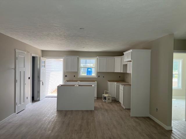 F Walton Rd, Kingsley, MI 49649 - kitchen featuring baseboards, a kitchen island, light wood-style flooring, white cabinetry, and a textured ceiling