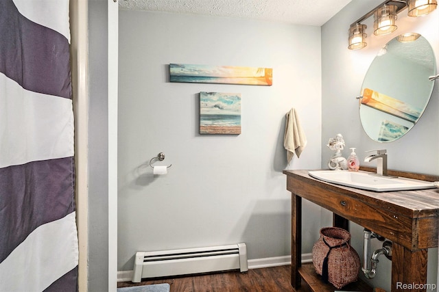 11135 Maple Ridge Way, Roscommon, MI 48653 - bathroom featuring a baseboard heating unit, wood finished floors, a textured ceiling, baseboards, and a sink