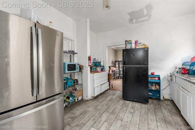 1475 Atkinson St, Detroit, MI 48206 - kitchen featuring freestanding refrigerator, white microwave, light wood-style flooring, and white cabinets