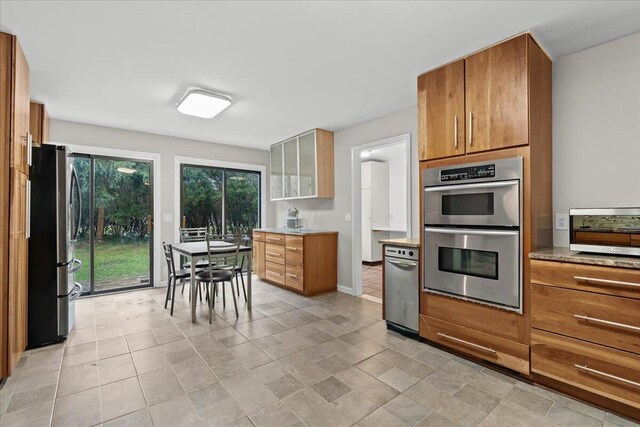 2128 Somerset Rd, Bloomfield Hills, MI 48302 - kitchen featuring stainless steel appliances, brown cabinets, glass insert cabinets, baseboards, and light stone counters