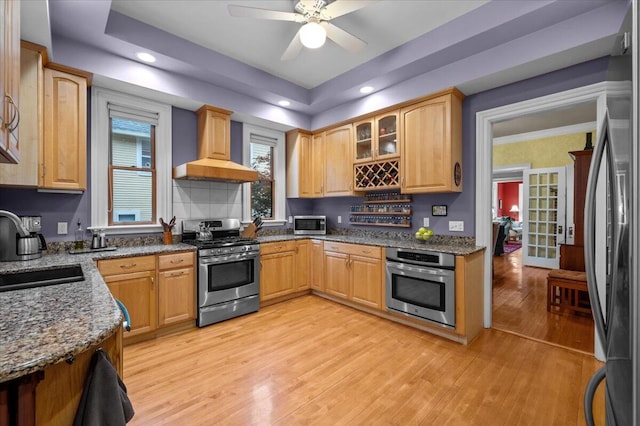 244 Paris Ave SE, Grand Rapids, MI 49503 - kitchen featuring stainless steel appliances, wall chimney range hood, a sink, dark stone counters, and light wood-type flooring