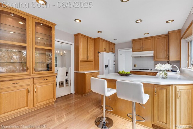 3379 Wormer Dr, Waterford, MI 48329 - kitchen with white fridge with ice dispenser, light wood-style floors, under cabinet range hood, light countertops, and decorative backsplash